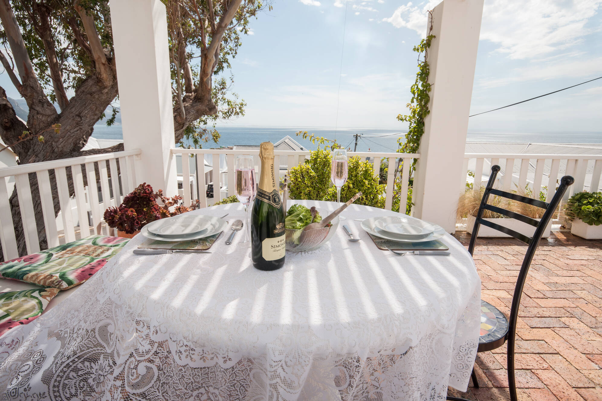 Outdoor dining table at Mermaid Rock Cottage with a bottle of champagne, set for two, overlooking the ocean with beautiful sea views in a Southern Peninsula holiday rental.