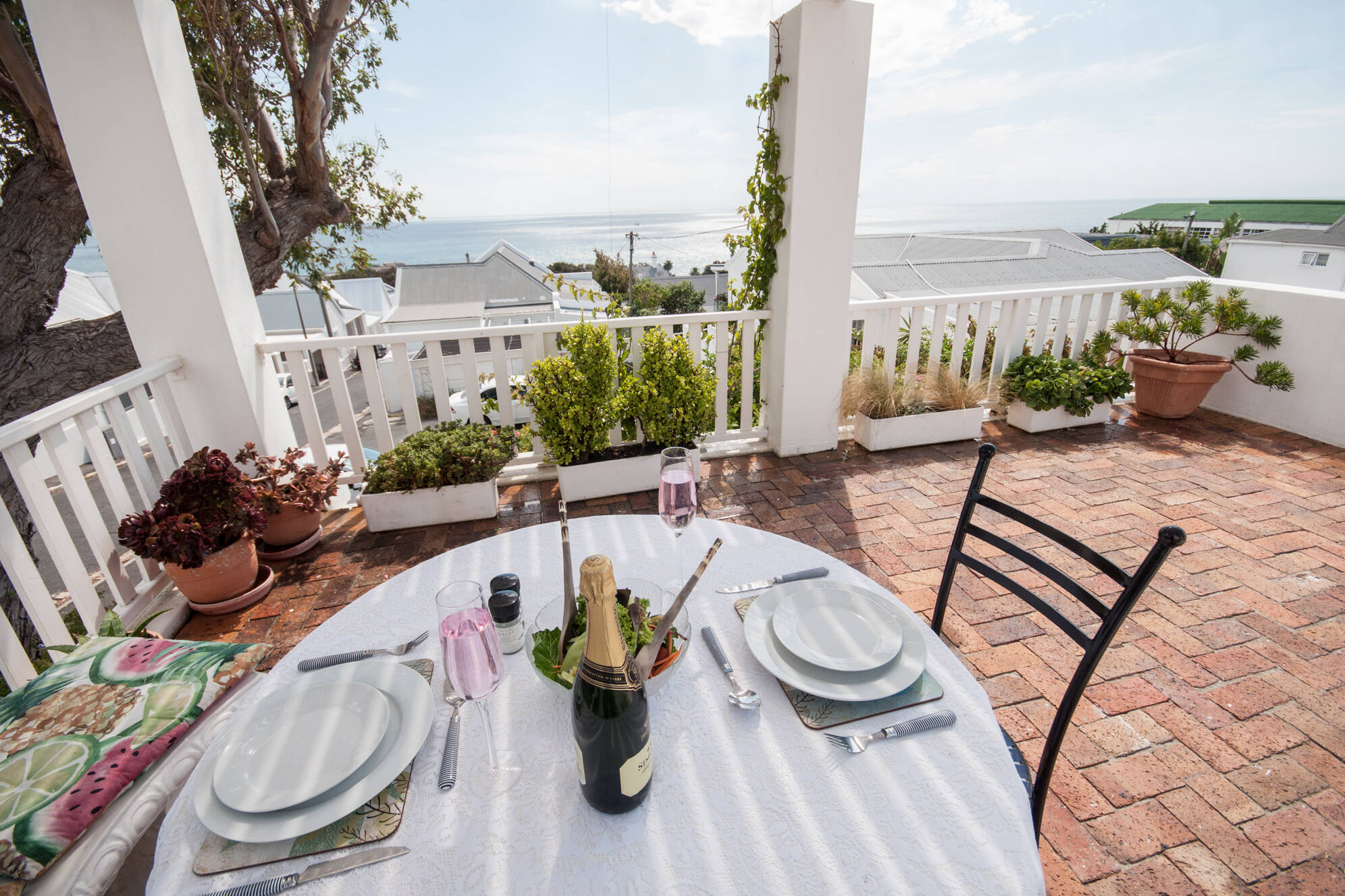 Outdoor dining table at Mermaid Rock Cottage set for two, with champagne and glasses, overlooking the ocean in Simonstown