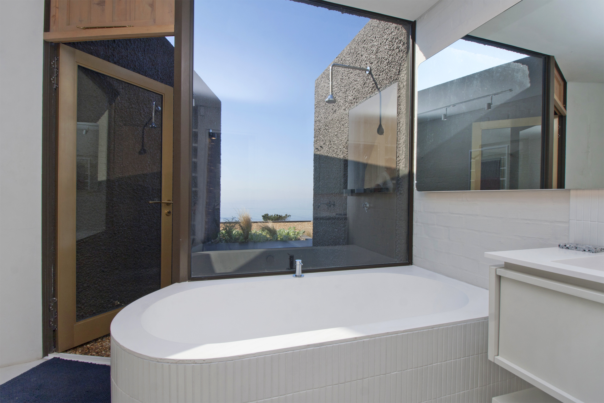 Modern bathroom with a sleek bathtub and large windows offering an outdoor view of a private shower and scenic surroundings.